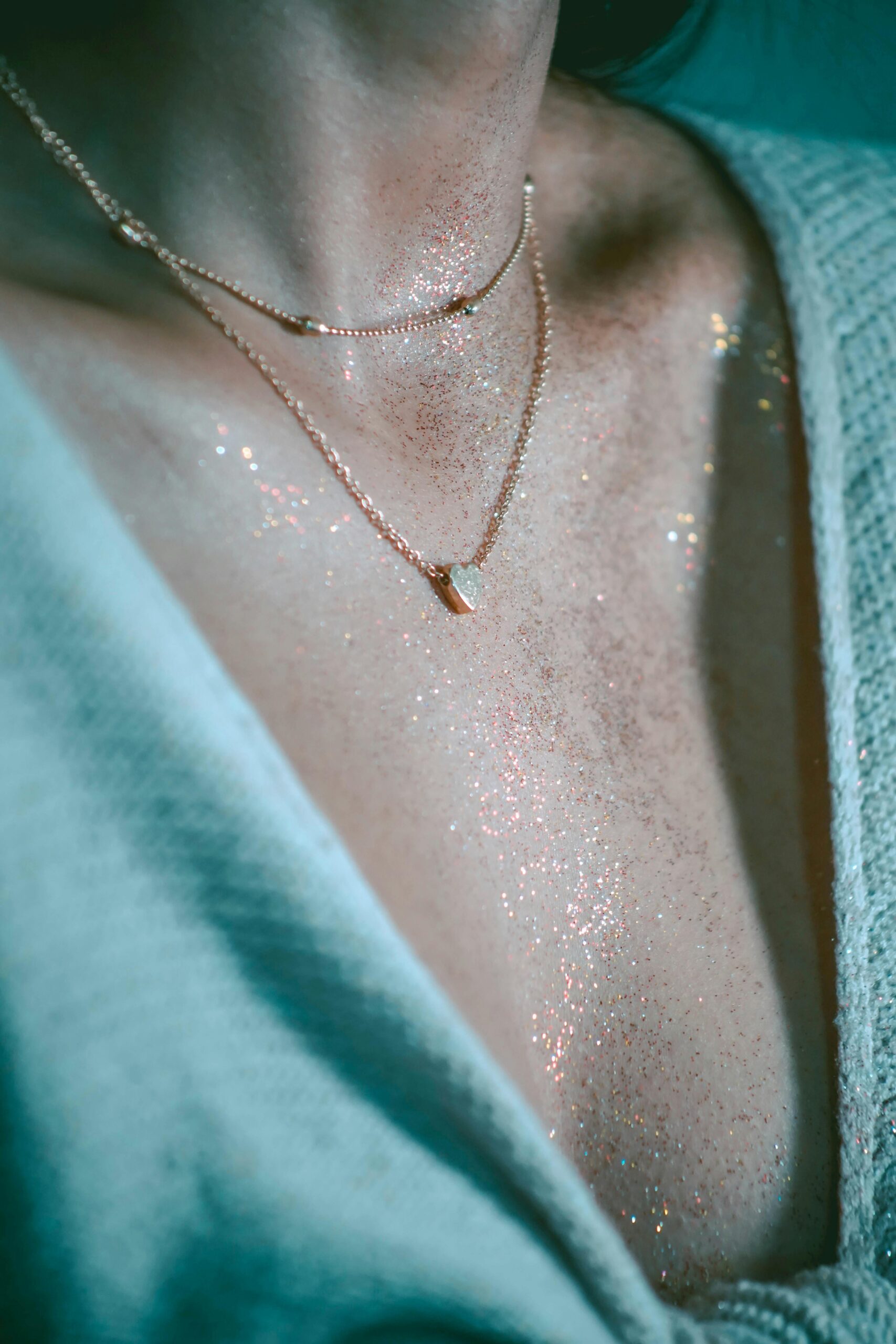 Close-up of a woman's neck adorned with glitter and delicate jewelry, creating a shimmering effect.